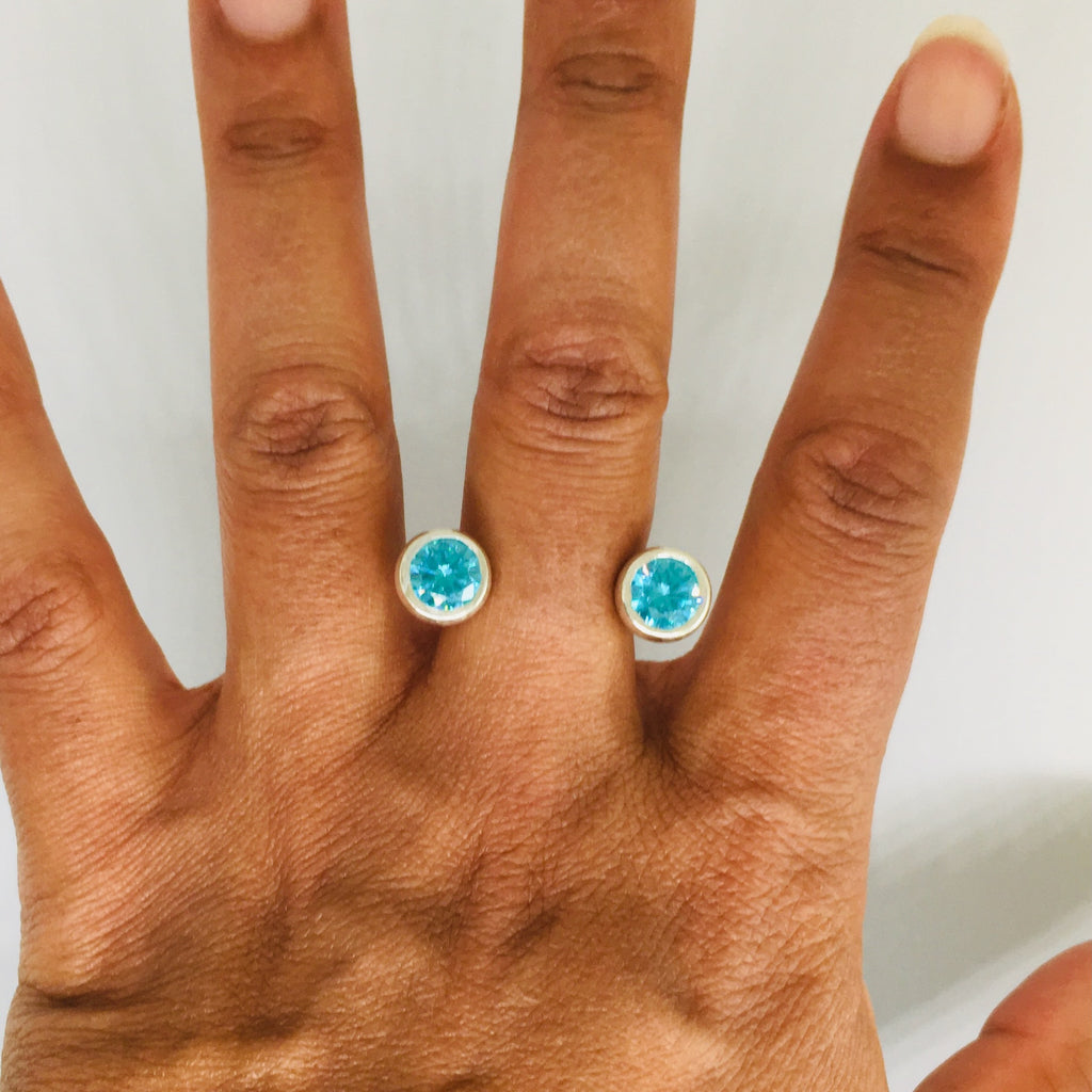 A hand wearing two sterling silver rings with blue topaz gemstones, arranged in a curved pattern resembling a crescent moon.